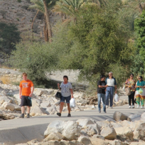 Oman Adventure Tour group walking along a rocky valley path surrounded by palm trees and desert hills in Oman.