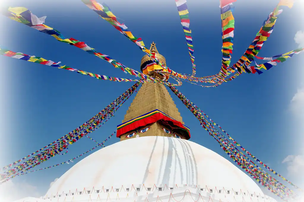 Boudhanath Stupa in Kathmandu with colorful prayer flags radiating outward against a clear blue sky.