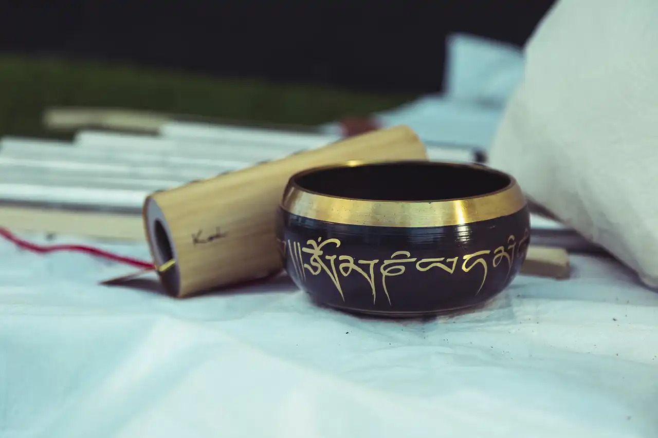 Traditional singing bowl with engraved mantra placed on a cloth, with a wooden striker beside it.
