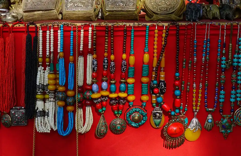 Colorful handmade necklaces with beads, stones, and pendants displayed on a red backdrop in a Nepali market.