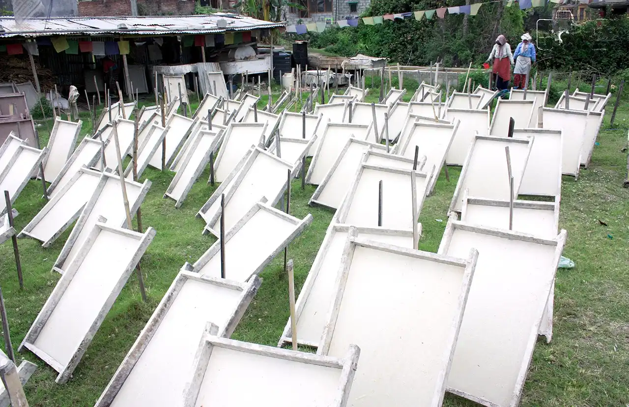 Handmade lokta paper sheets drying outdoors on wooden frames in a traditional Nepali paper workshop.