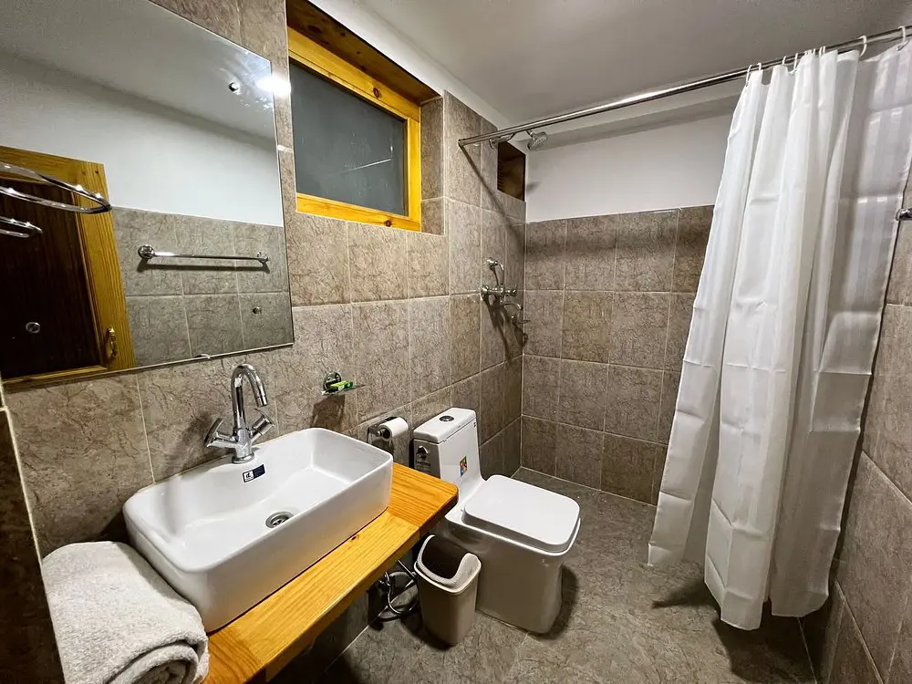 A clean, modern bathroom with tiled walls, a white sink, toilet, shower area with a curtain, and a small window.