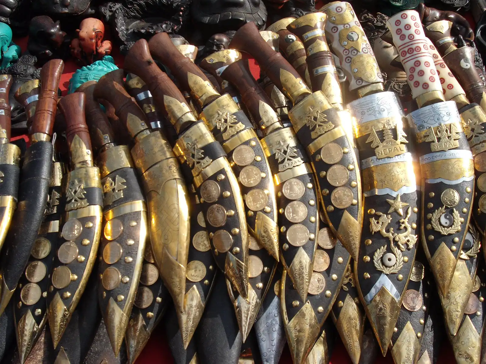 A collection of traditional Nepalese Khukuri knives with ornate gold and black scabbards, displayed in a market.