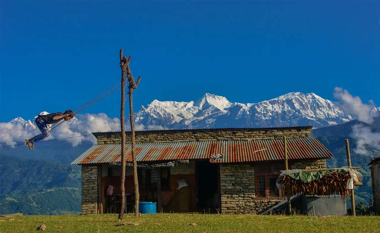 A young boy swings on a traditional swing in Thulakot, Nepal, with the Himalayas in the background during Dashain Festival.