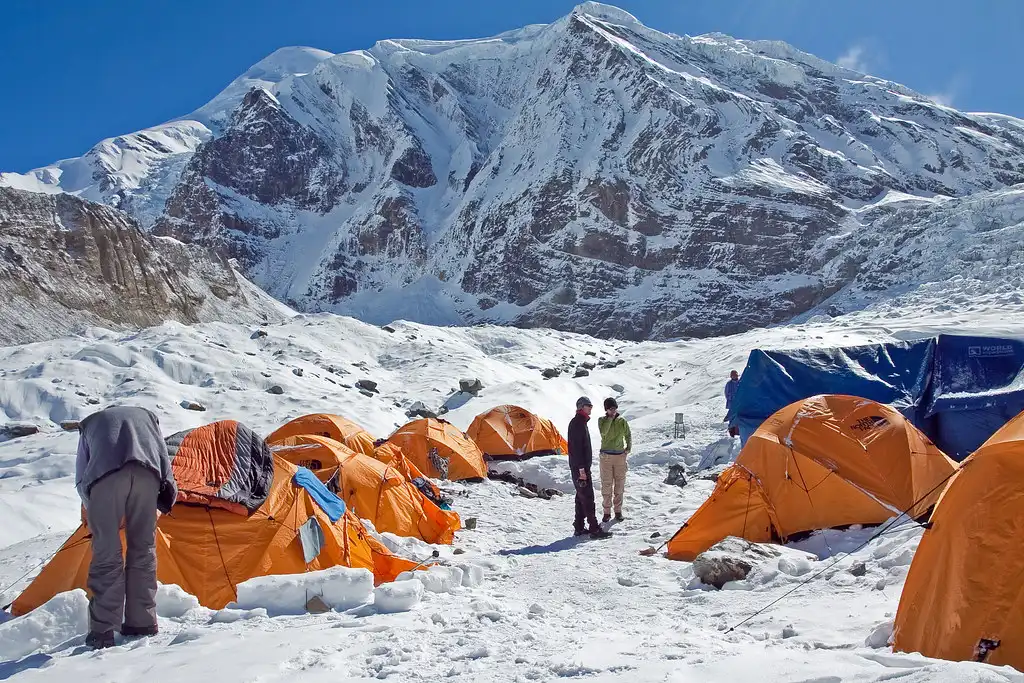 Campsite at Dhaulagiri Base Camp with tents set up on snowy ground and Dhaulagiri mountain in the background.