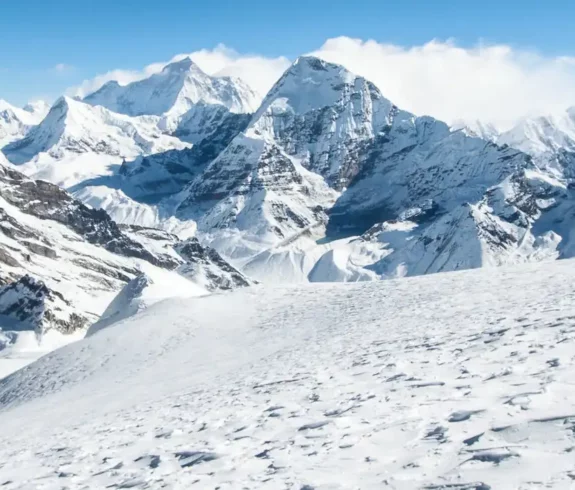 ヒマラヤ山脈のパノラマビューを眺めながら、雪景色の中をトレッキングしながらチュル西峰を登る登山者の列。