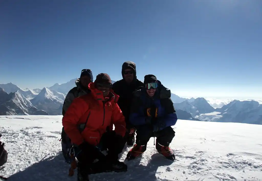A group of climbers standing on the summit of Mera Peak with snow-covered Himalayan peaks in the background.