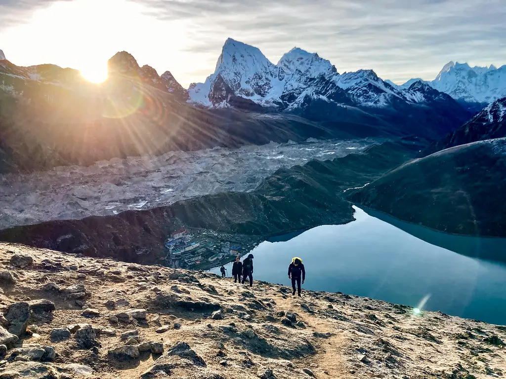 Trekkers climbing Gokyo Ri at sunrise with golden light over Gokyo Lake, Ngozumpa Glacier, and surrounding Himalayan peaks.