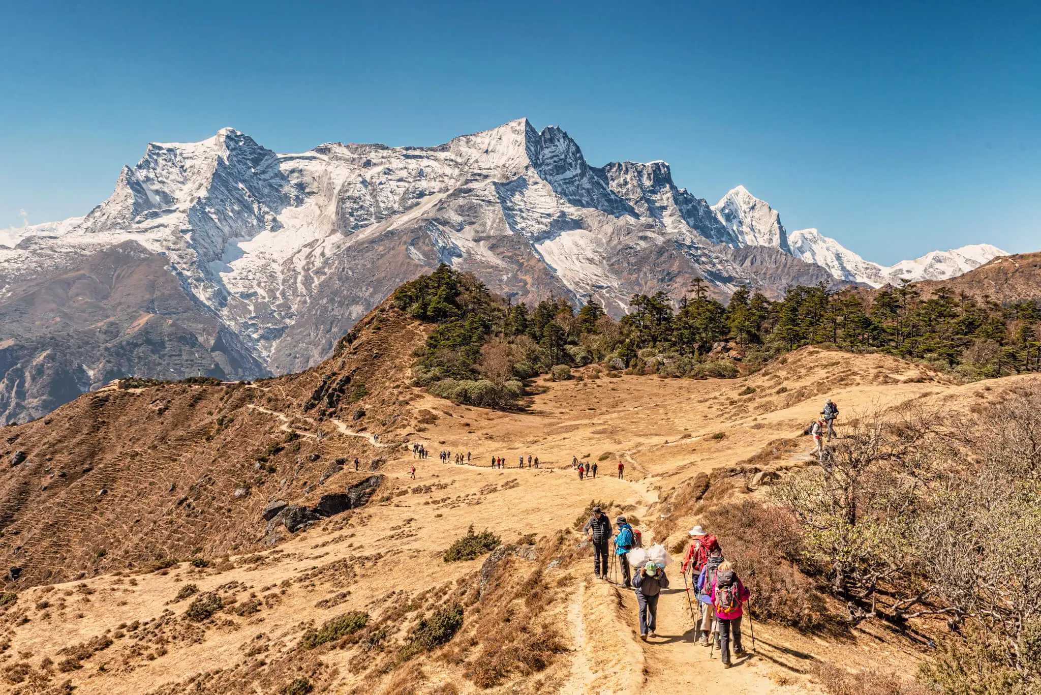 Tourists on the trekking route to Everest Base Camp just outside of Namche Bazar on the way to Everest view Hotel Kongde Ri peak at the background.