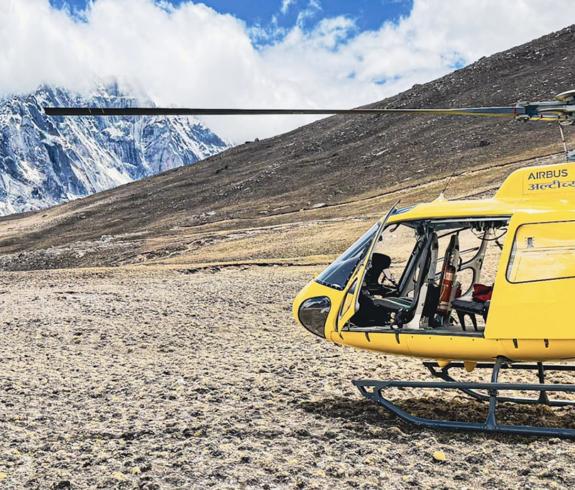Airbus AS350 helicopter landed at high altitude near Everest with trekkers and Himalayan peaks in background — Peregrine luxury EBC trek helicopter return