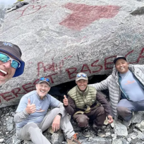 A group of happy hikers and their local guides taking a celebratory selfie in front of the iconic painted rock landmark at the completion of their Luxury Everest Base Camp Trek with Helicopter Return in Nepal.
