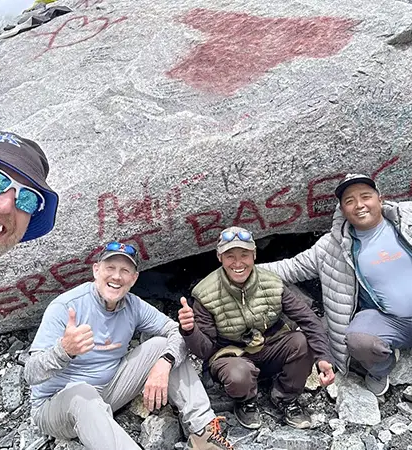 A group of happy hikers and their local guides taking a celebratory selfie in front of the iconic painted rock landmark at the completion of their Luxury Everest Base Camp Trek with Helicopter Return in Nepal.