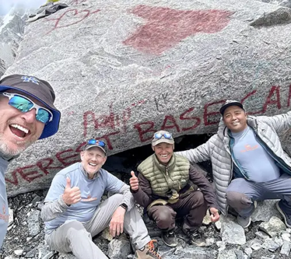 Eine Gruppe glücklicher Wanderer und ihre einheimischen Führer machen ein Selfie zur Feier des Tages vor dem ikonischen bemalten Felsen als Wahrzeichen nach Abschluss ihrer Luxus-Trekkingtour zum Everest-Basislager mit Helikopterrückflug in Nepal.