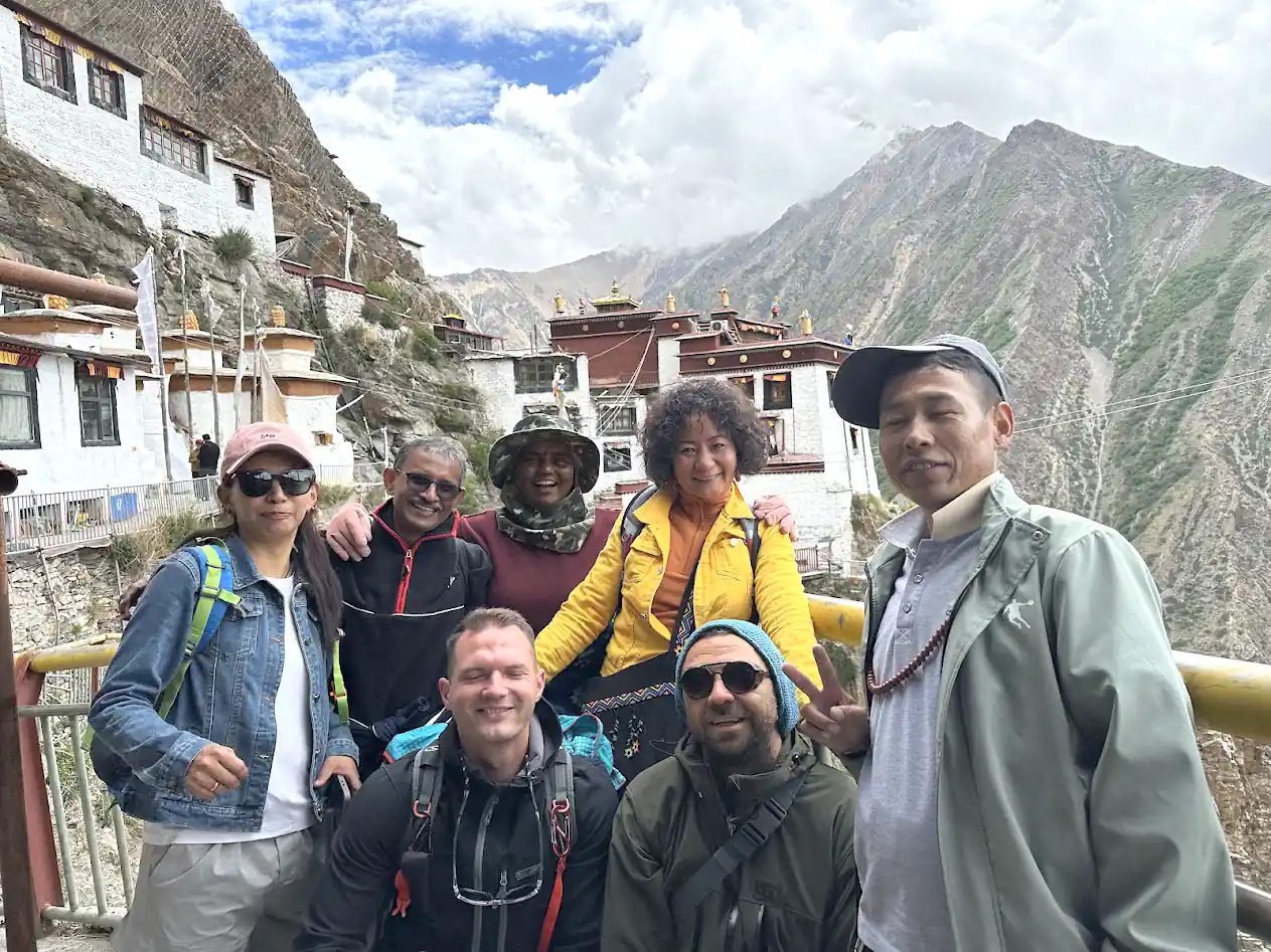 Eine Gruppe unterschiedlicher Touristen lächelt und posiert vor der Milarepa-Höhle, umgeben von einer rauen Berglandschaft.