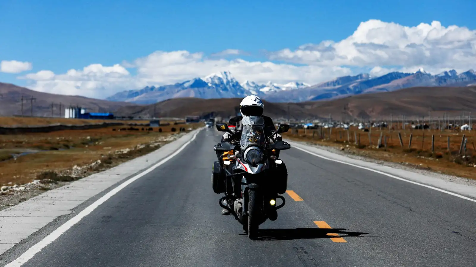 摩托车手在西藏的一条开阔道路上行驶，背景是群山。
