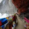 Narrow trail on the Kailash Inner Kora lined with colorful prayer flags against a dramatic cliffside.