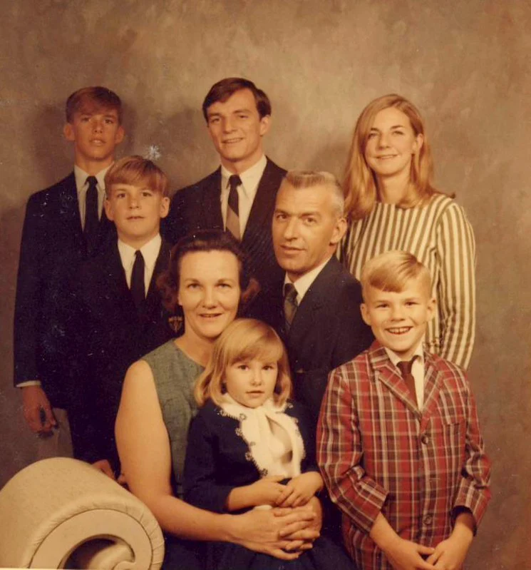 A vintage family portrait featuring eight members dressed in formal attire, with Pema Chödrön as a young girl in the front row.