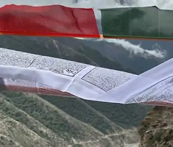 Bunte tibetische Gebetsfahnen flattern vor der Kulisse einer Berglandschaft.