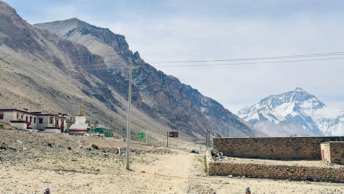 View of Rongbuk Monastery with Mount Everest in the background, featuring a stupa and traditional Tibetan buildings under a clear sky.