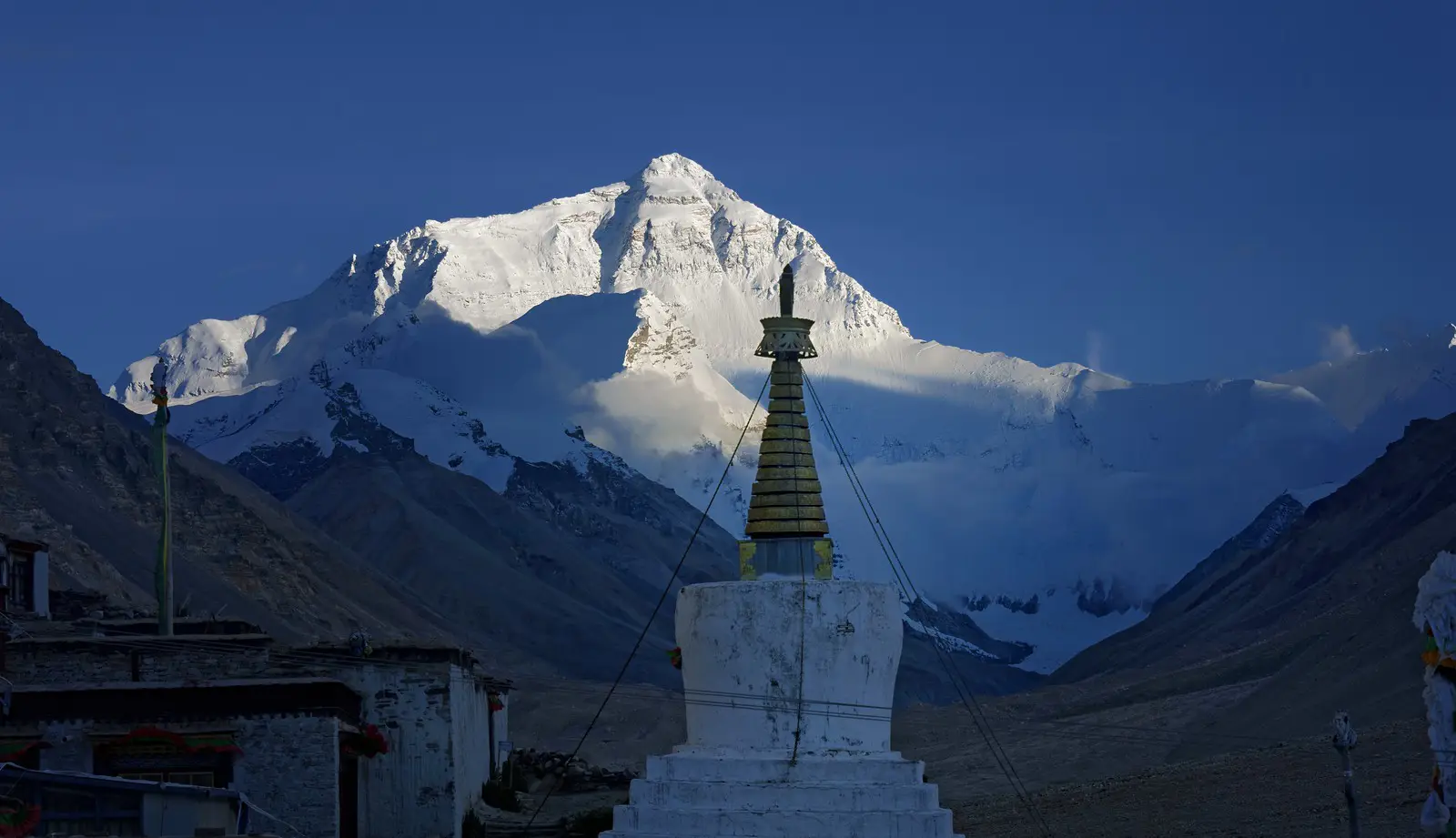 View of Mount Everest from Rongbuk Monastery in Tibet, with a traditional white stupa in the foreground against a backdrop of the snow-covered mountain under a clear blue sky.