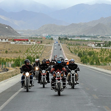 A group of motorcyclists on a highway in Tibet, surrounded by majestic mountains during Tibet Motorbike Tour