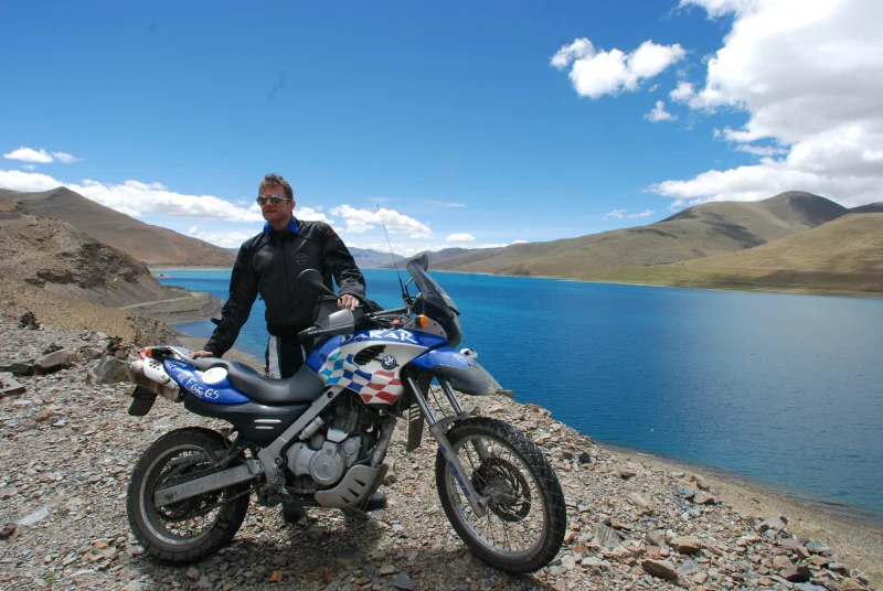 摩托车手在西藏美丽的羊卓雍错湖旁与自行车合影。
