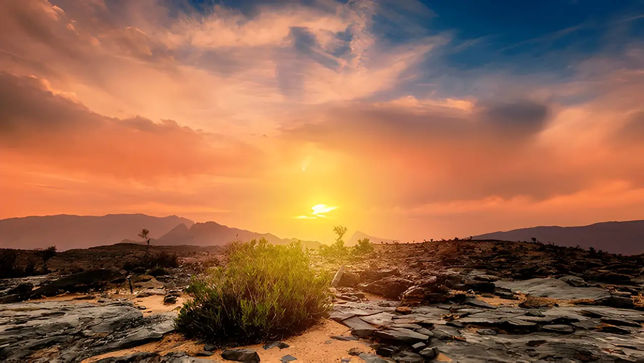 Beautiful view of a sunset from a plateau on Jebel Shams Mountain in Oman, with the sky painted in vibrant orange hues and rocky terrain in the foreground.