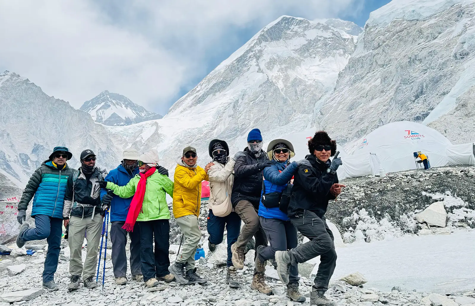 A joyful group of seven trekkers posing together in a playful manner against a backdrop of snowy Himalayan mountains at Everest Base Camp.