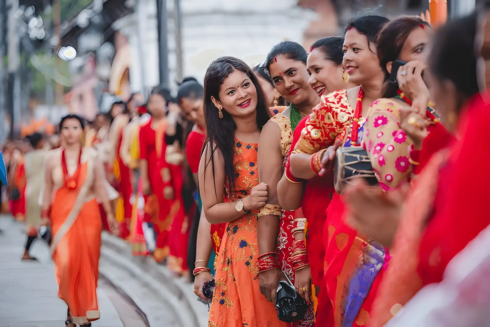 A group of Nepali Hindu women in colorful traditional attire, smiling and engaging with each other while waiting in line at Pashupatinath Temple.