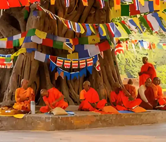 Buddhist monks meditating under a tree adorned with colorful prayer flags in Lumbini, Nepal, during Buddha Purnima.