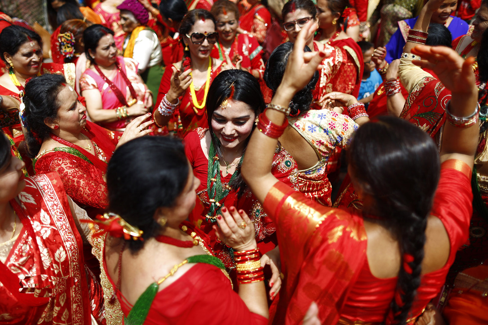 Nepalese Hindu women in vibrant red sarees joyfully dancing and singing during the Haritalika Teej festival at Pashupatinath Temple.