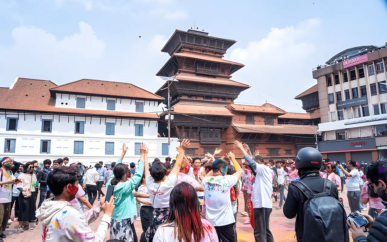 Celebrants joyfully throwing colors during the Holi Festival in Kathmandu, Nepal, with a traditional pagoda-style building in the background.