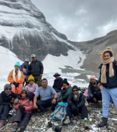 A group of trekkers, known as the Peregrine Team, at Charan Sparsh, with the snow-covered Mount Kailash in the background.