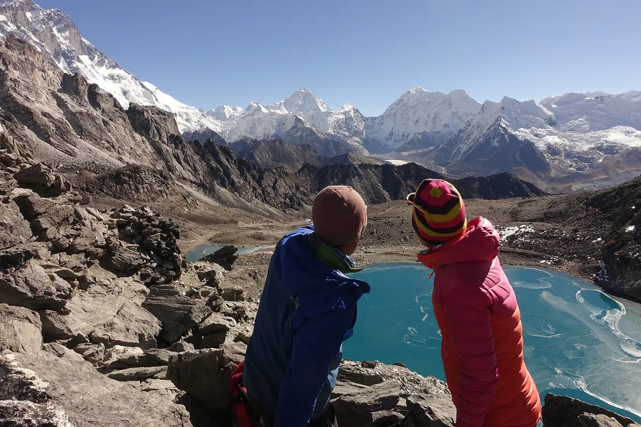 Two hikers gazing at a stunning turquoise lake surrounded by rugged mountains at Kongma La Pass.