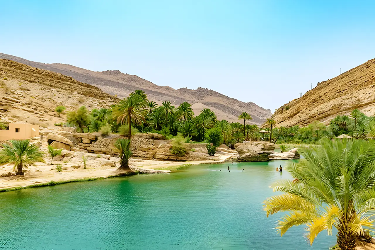 Wadi Bani Khalid in Oman, featuring a tranquil turquoise pool surrounded by palm trees and rocky desert mountains.