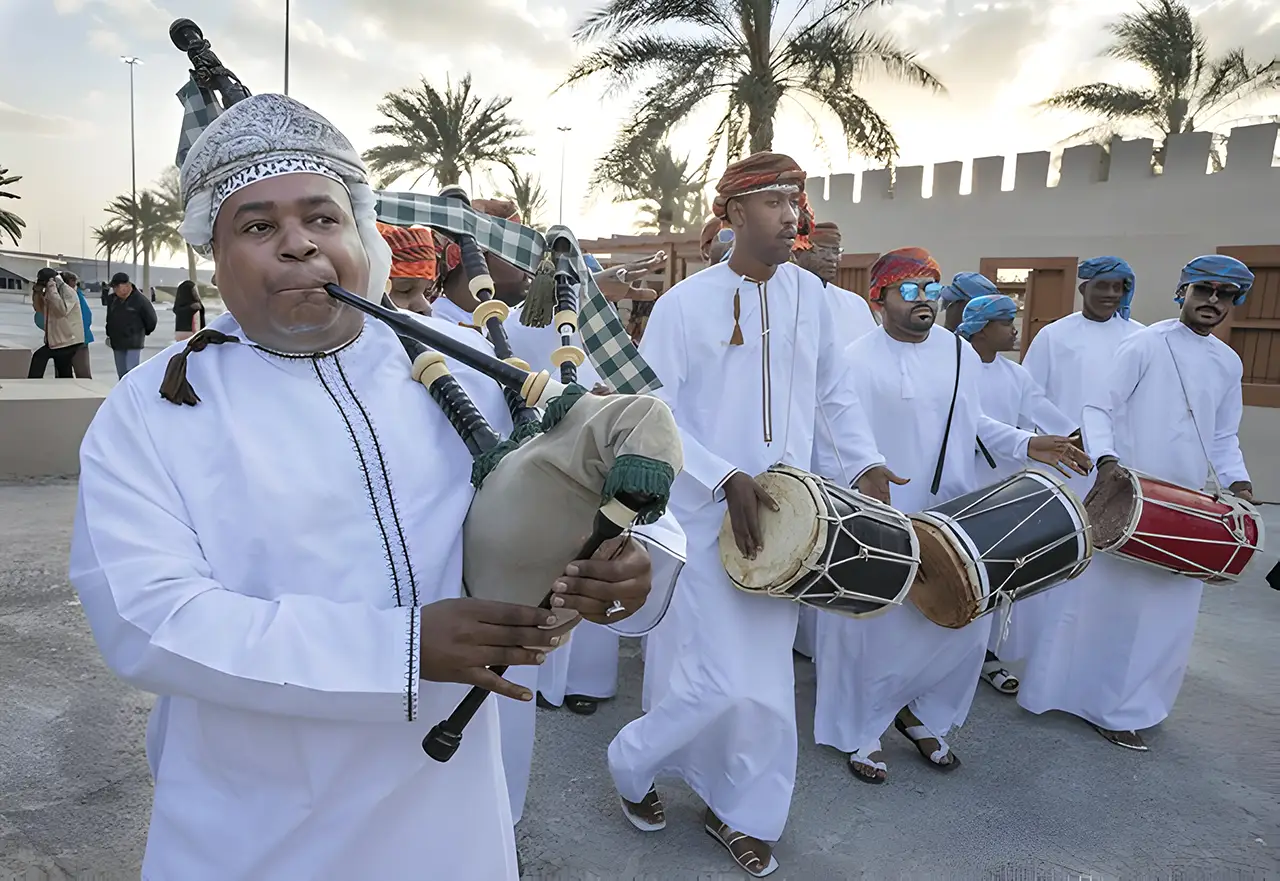 Omani men celebrating with traditional songs and dances, featuring musicians playing drums and a bagpipe, dressed in traditional white dishdashas.