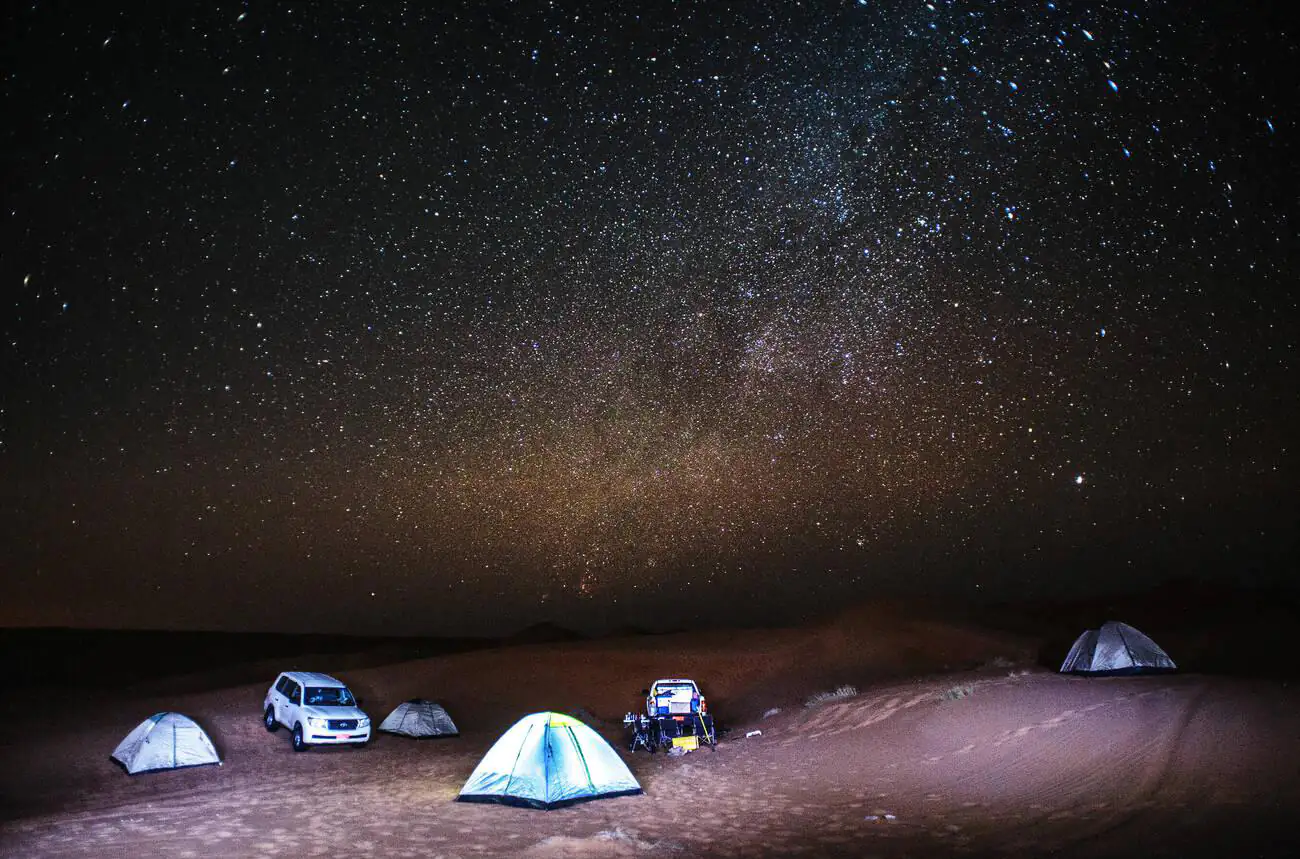 A breathtaking night sky filled with stars over camping tents and vehicles in the Wahiba Sands desert in Al Sharqiya, Oman.