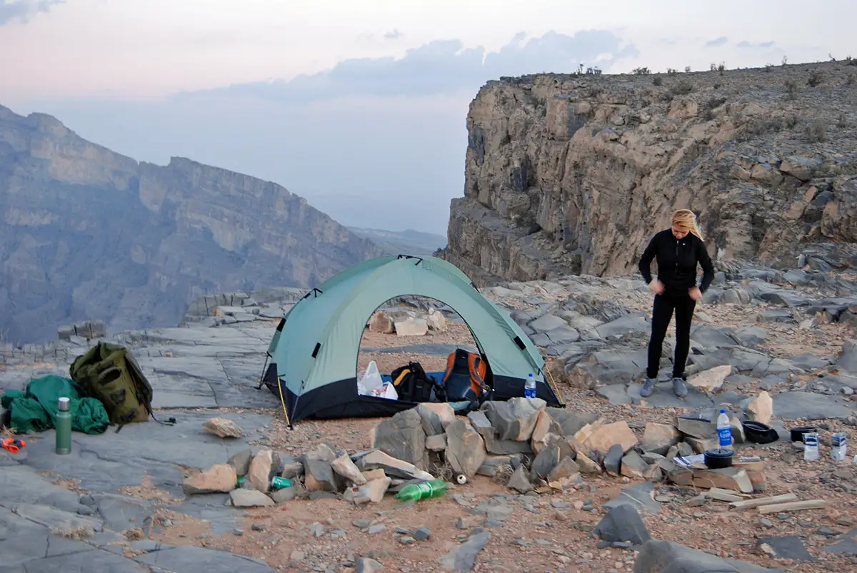 Camping setup on Jebel Shams in Oman, with a tent and hiker amidst a rocky mountainous landscape.