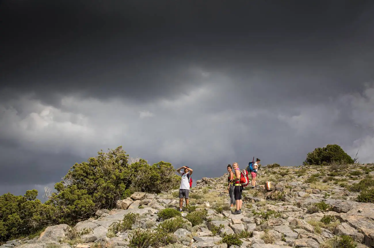 Hikers trekking in the mountains near Jebel Shams, Oman, under a cloudy sky.