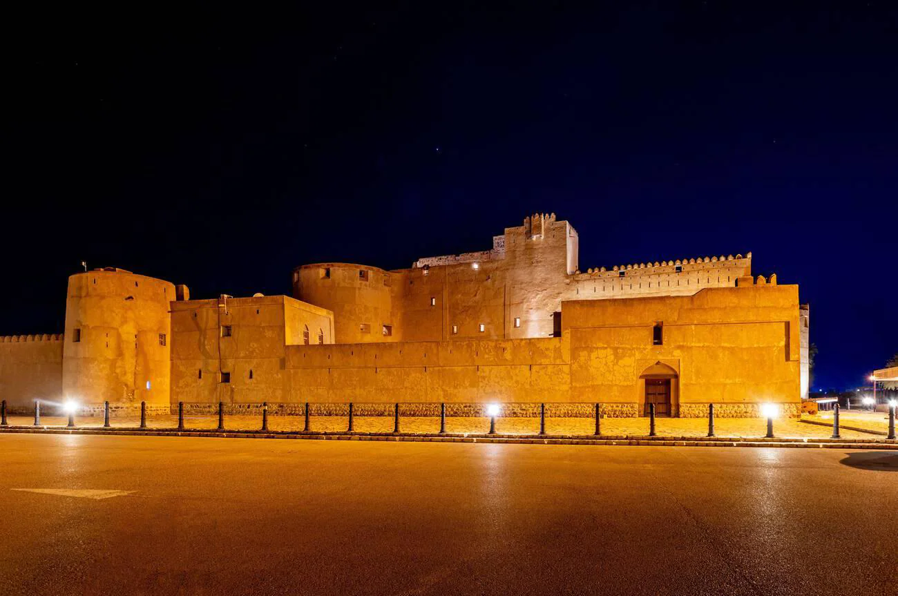 Jabreen Citadel illuminated at night, showcasing its robust stone walls and round bastion towers in Bahla, Oman.