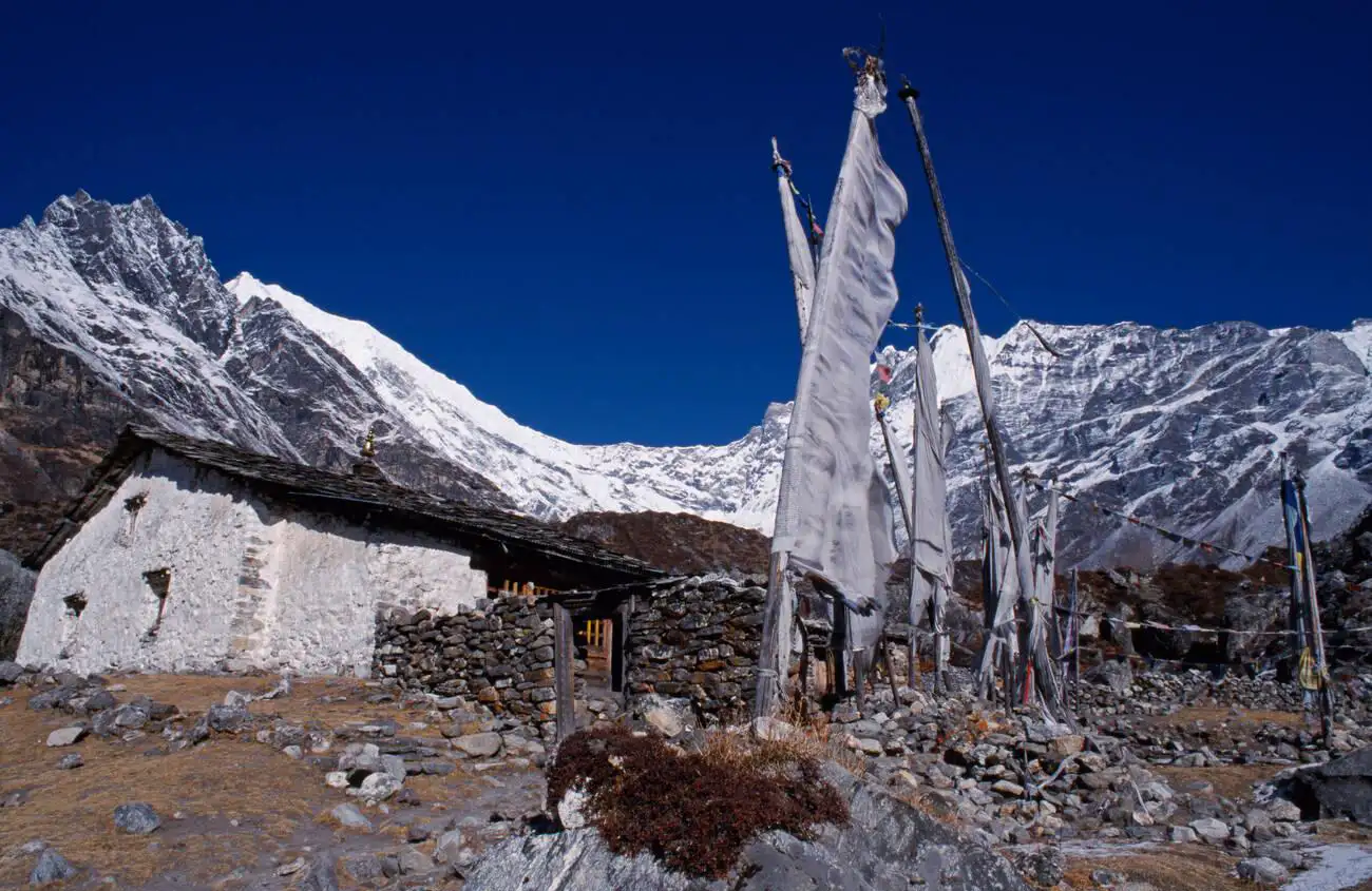 A traditional stone monastery with prayer flags at Kyangjin Gompa, set against the snow-capped peaks of Langtang Lirung in Nepal.