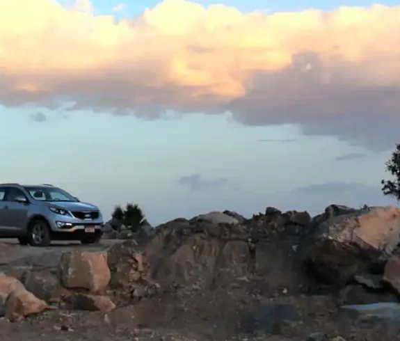 Landscape view of a SUV on a mountain path with trees and sunset clouds