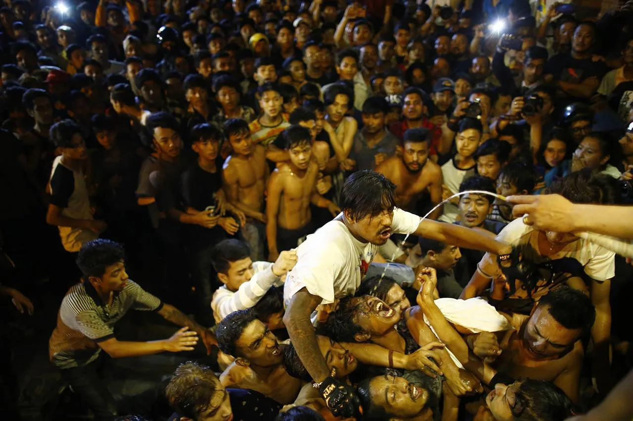 Nepalese youths struggling to drink alcohol from the mouth of the Swet Bhairav deity during the Indra Jatra festival in Kathmandu, Nepal.