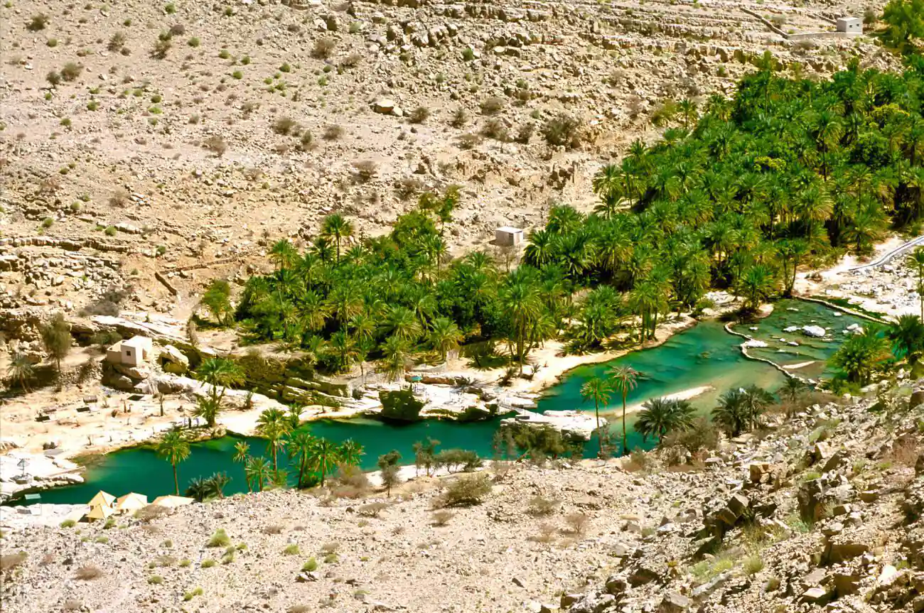 Lush date palms surround the tranquil rock pools of Wadi Bani Khalid nestled in the Eastern Hajar mountains of Oman.