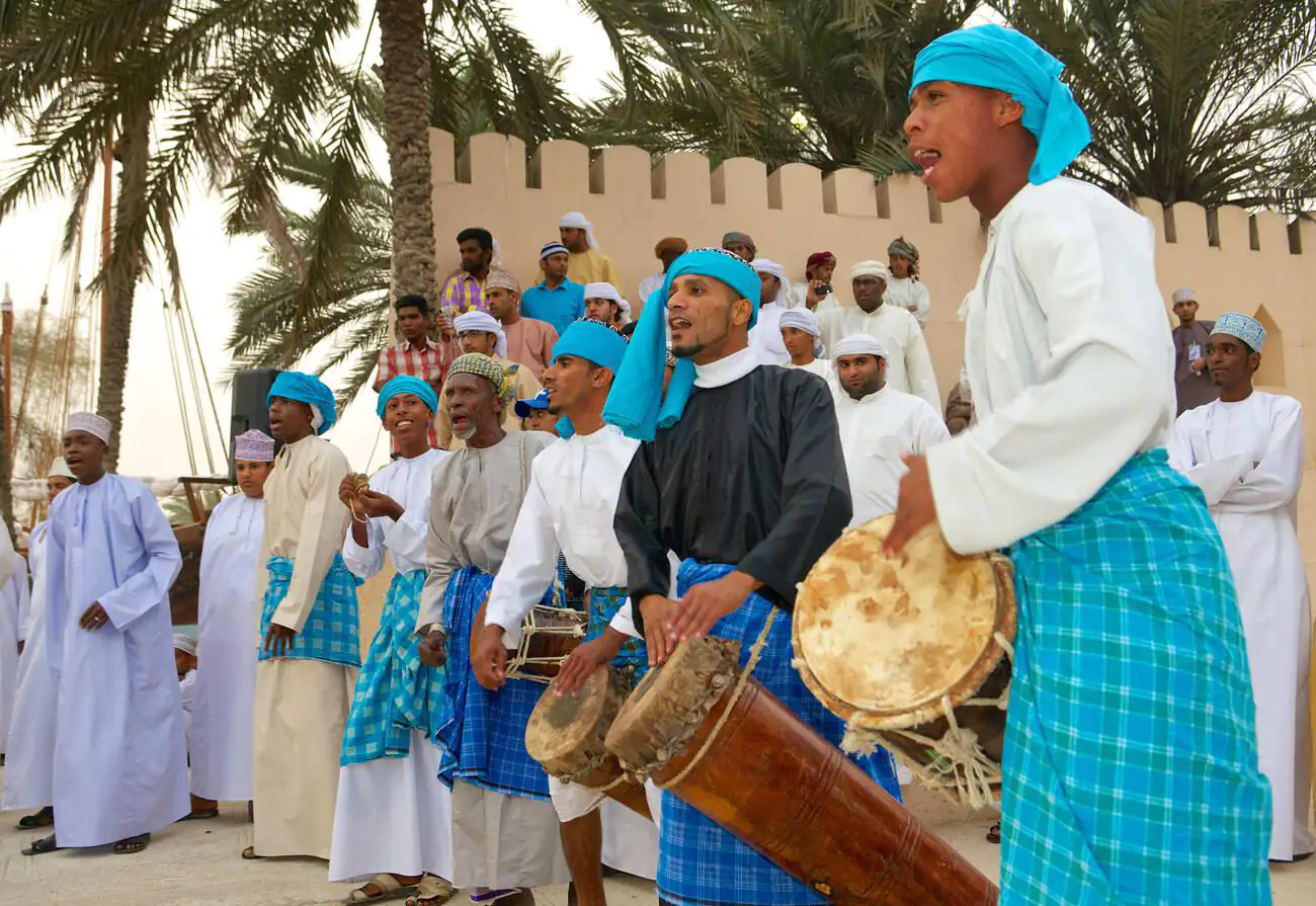 Omani musicians perform during a tribal dance at the Muscat Festival, clad in traditional attire and playing indigenous instruments.