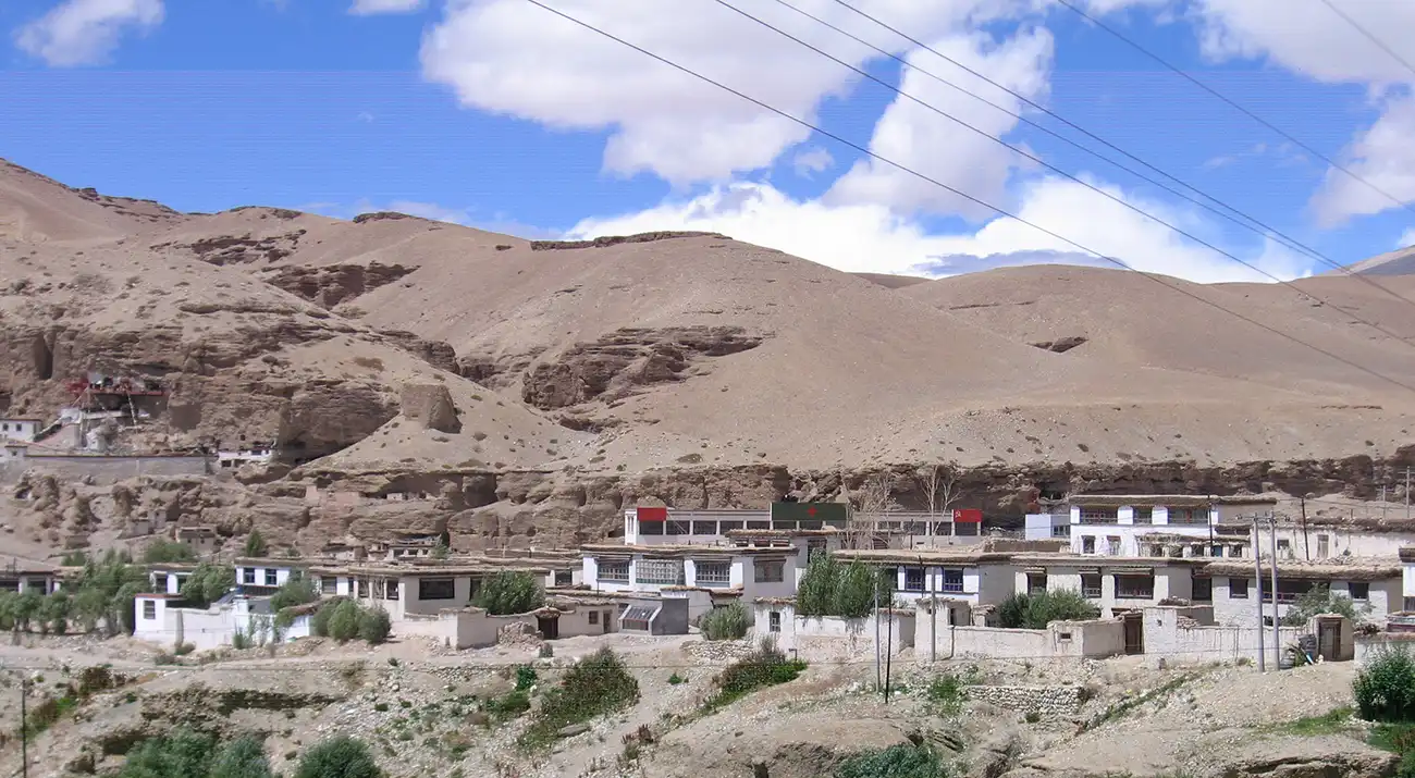 Een klein dorpje vlakbij de stad Taklakot, omgeven door kale heuvels en weinig groen, onder een gedeeltelijk bewolkte hemel.