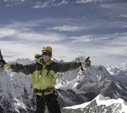Climber standing triumphantly at the summit of Island Peak with ice axe raised, surrounded by snow-capped Himalayan mountains.