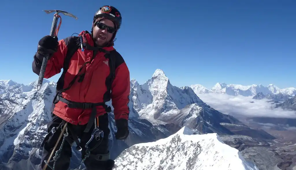 Climber standing on the summit of Island Peak at 6,189 meters, holding an ice axe with the stunning Himalayas in the background.