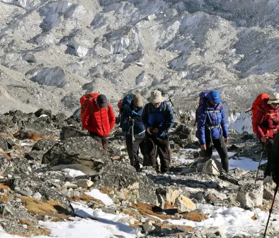 A group of climbers making their way into High Camp at Island Peak, navigating a rocky and snowy terrain with the towering Himalayas in the background.
