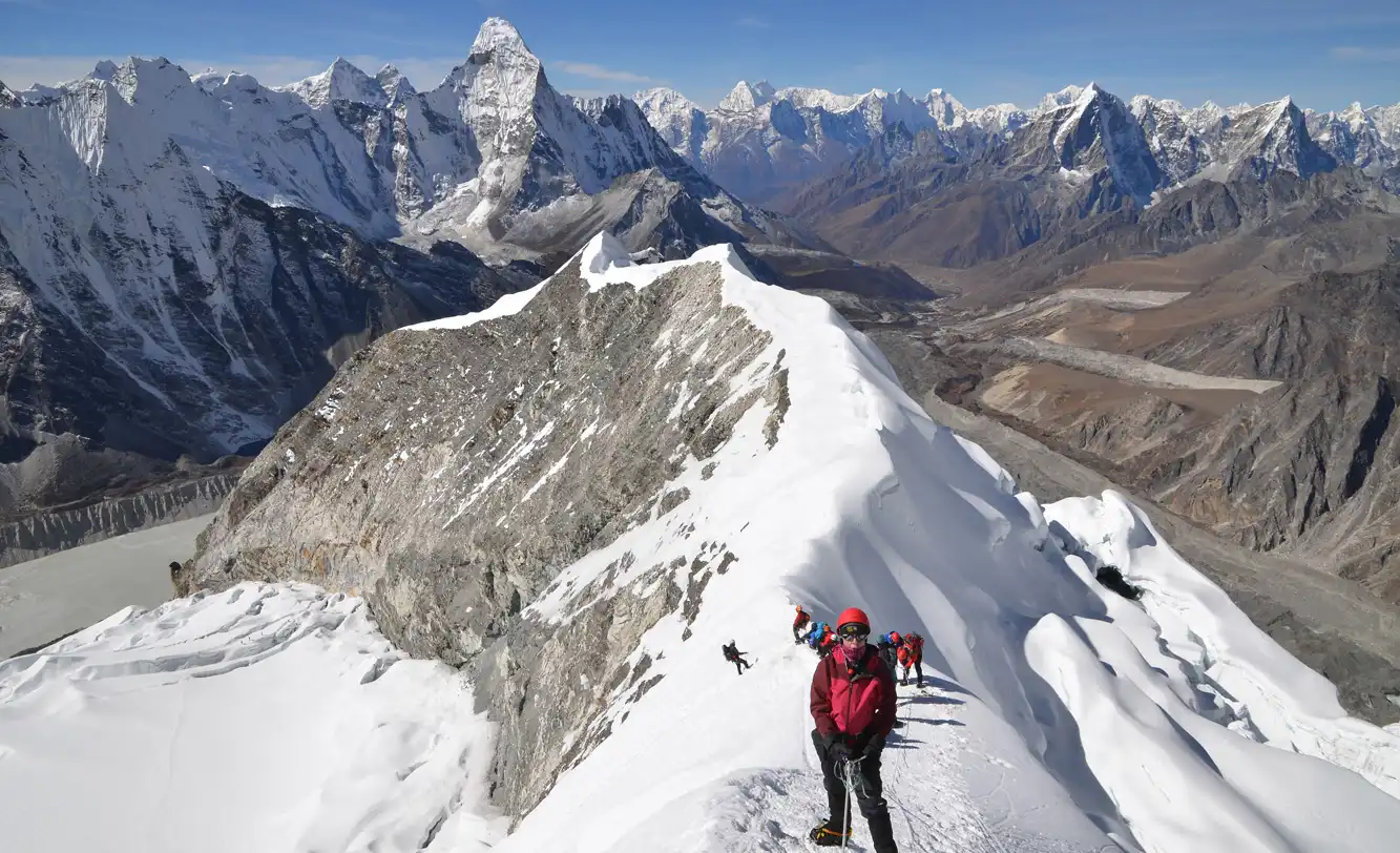 A group of climbers roped together ascending the snowy ridge of Island Peak, surrounded by towering Himalayan peaks under a clear blue sky.